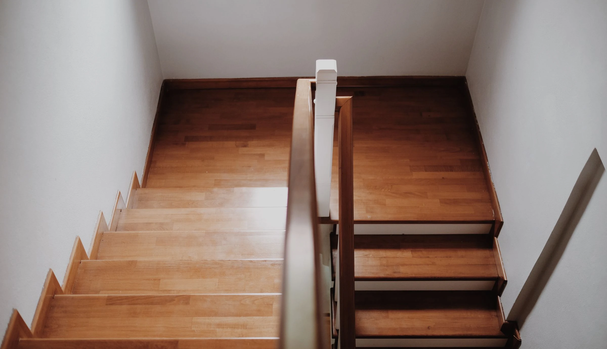 Un escalier en bois clair à deux volées, vu d'en haut, dans une cage d'escalier blanche
